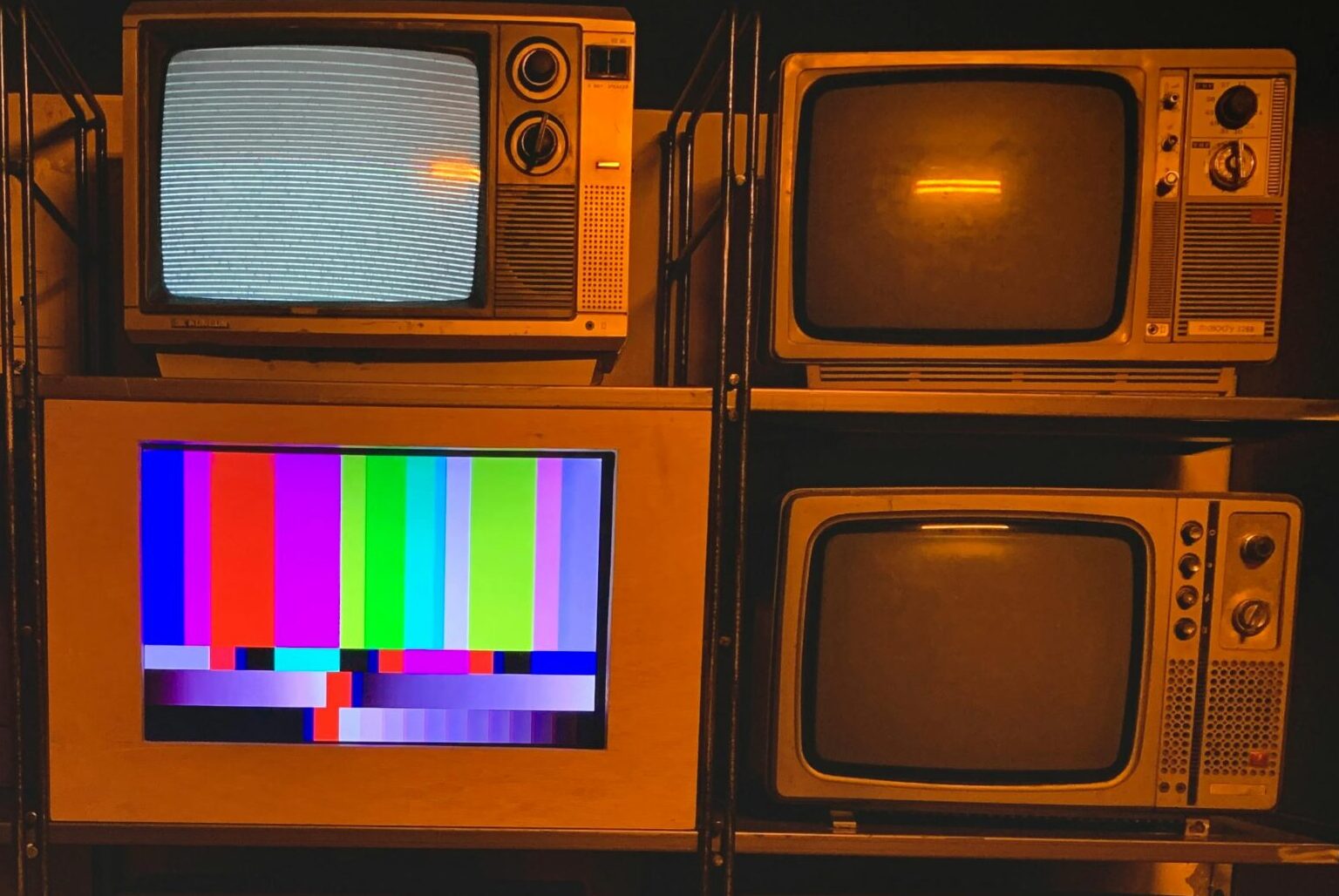 A collection of vintage televisions featuring static and color test patterns on the screens.